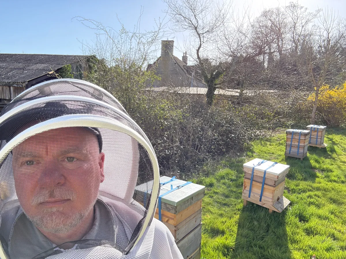 Scotty wearing his beekeeper’s veil beside his garden hives